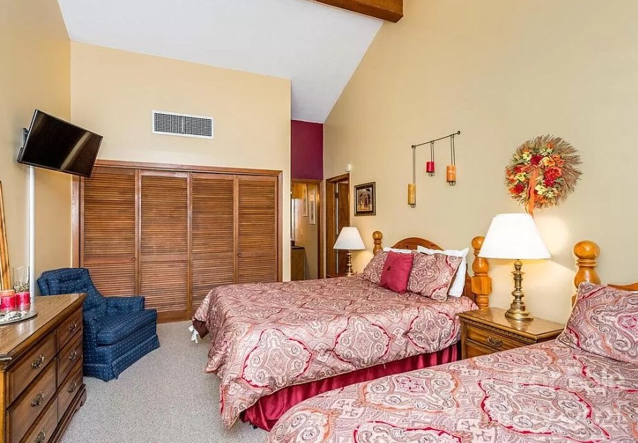 Lake Lure bedroom before the redesign, with beige walls, wood louvered closet doors and two beds in patterned bedding