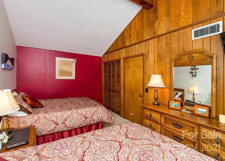 Lake Lure bunk room before the redesign, with wood-paneled walls, a red accent wall and two beds in patterned bedding