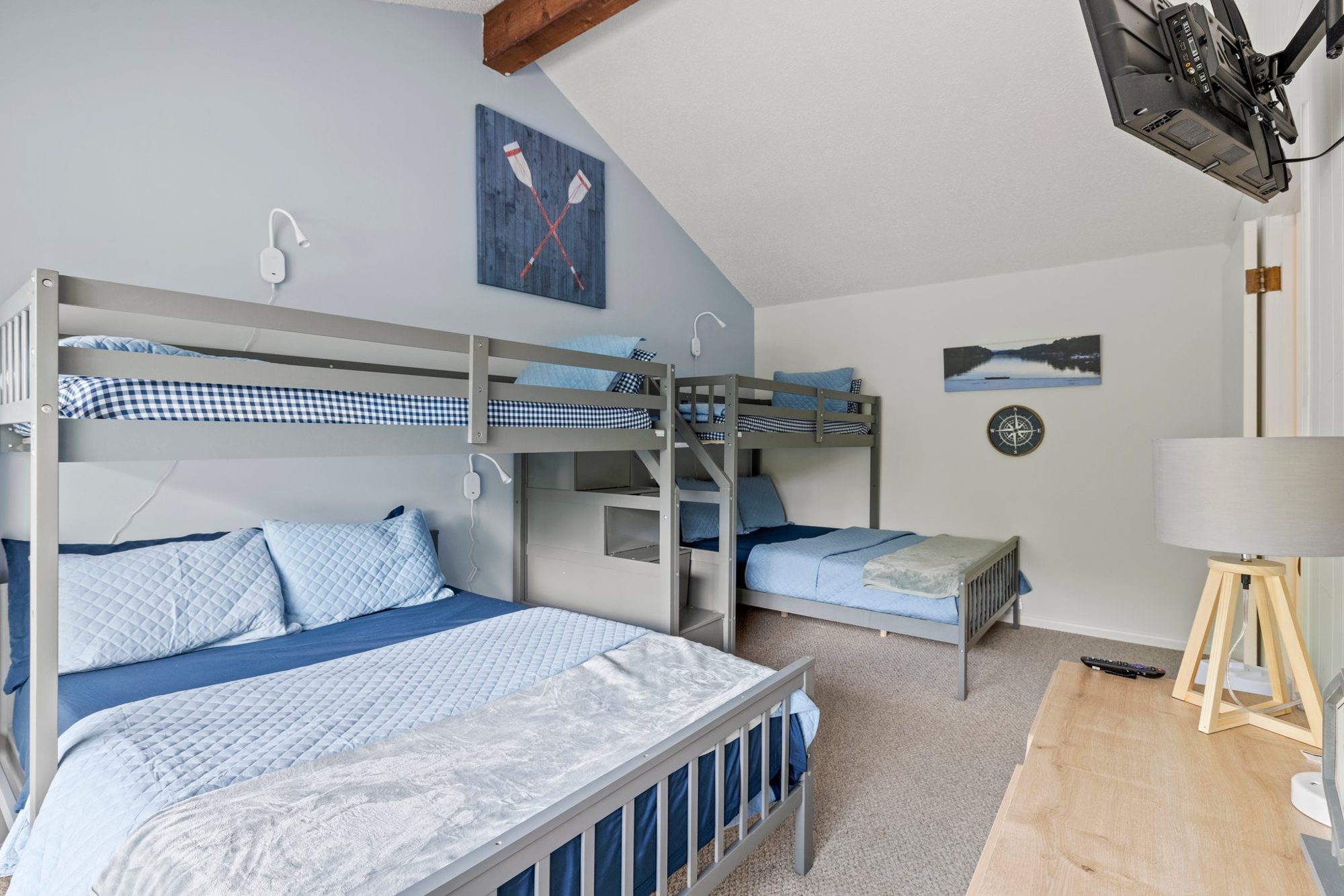 The same Lake Lure bunk room after the redesign, with soft blue walls, two gray bunk beds and a reading light at every bed