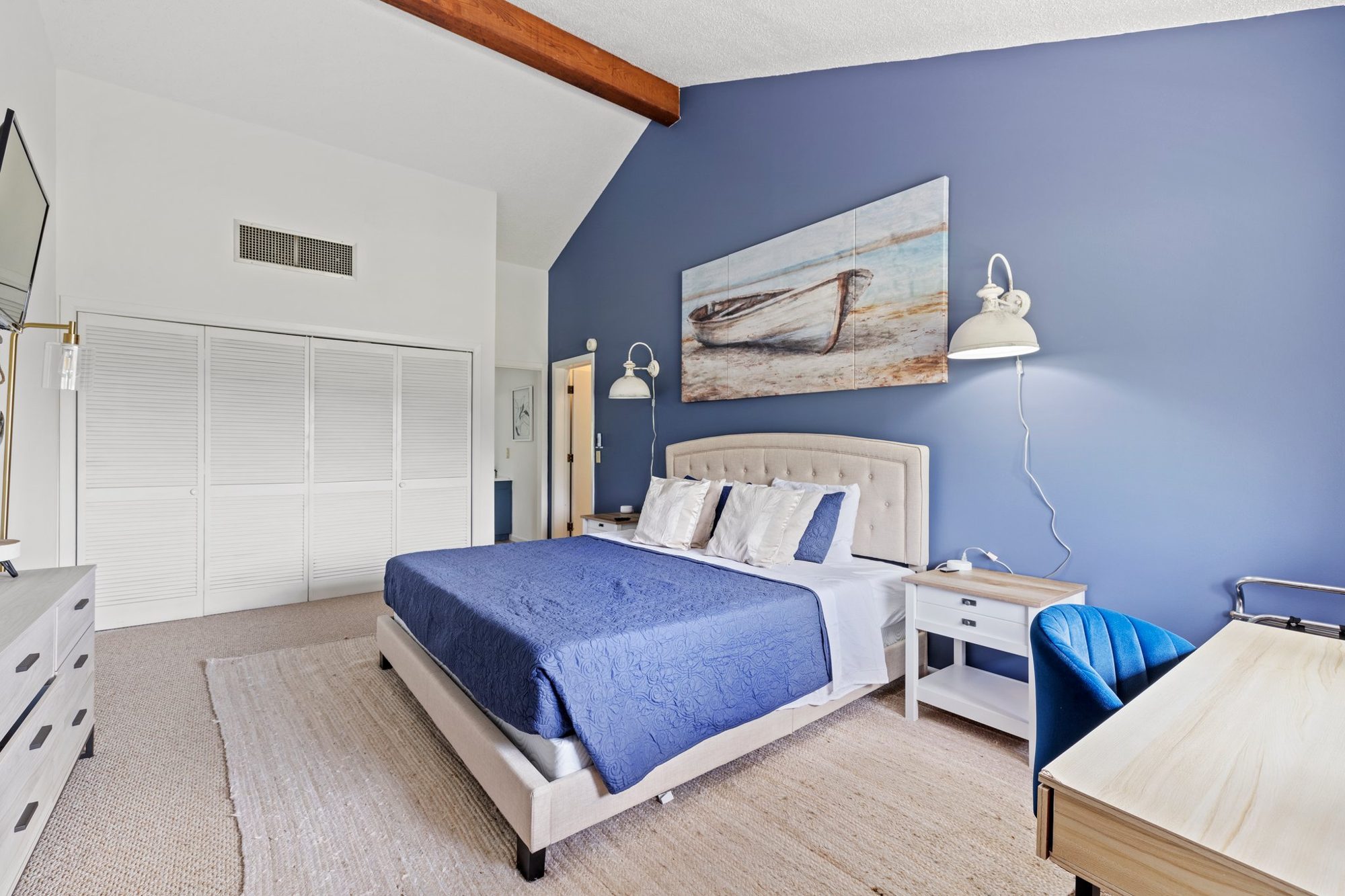 The same Lake Lure bedroom after the redesign, with white walls, a deep blue accent wall, one bed with an upholstered headboard and wall sconces